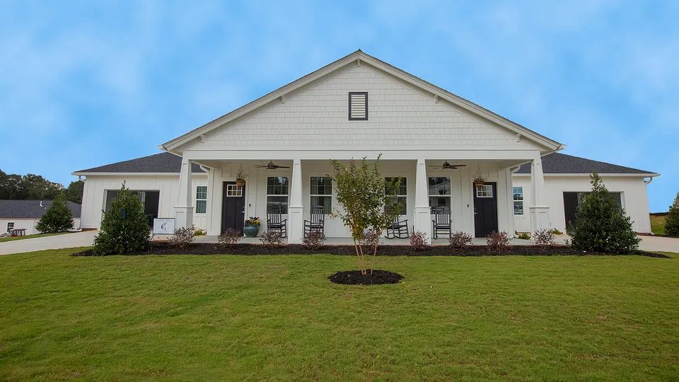 Charming modern farmhouse with inviting front porch, surrounded by lush green lawn and bright blue sky.