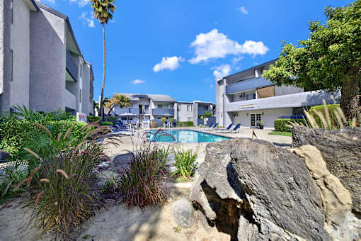 A pool surrounded by rocks and plants with a building in the background.