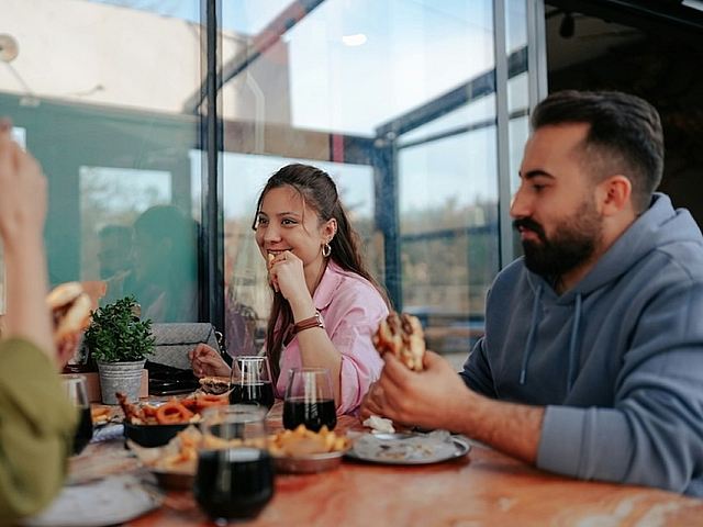 Cheerful group enjoying a meal together in a bright, modern dining area with glass walls and stylish decor.