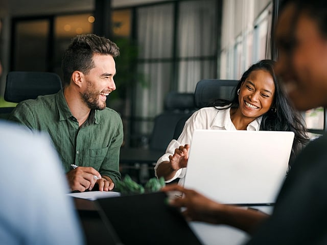 Vibrant office meeting scene with a diverse group of professionals sharing ideas and smiles around a table, creating a dynamic and inspiring workspace.