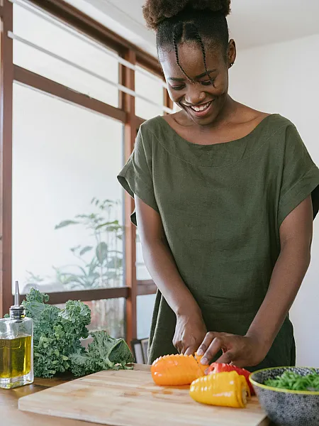 A woman cutting bell peppers and kale in the kitchen