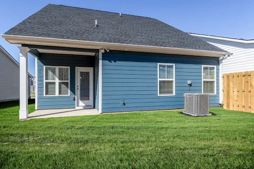 A blue house with a patio, air conditioning unit, and green lawn under a clear blue sky.