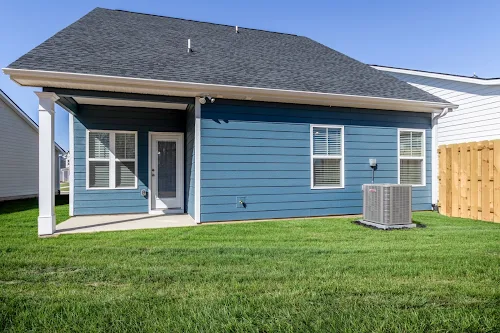 A blue house with a patio, air conditioning unit, and green lawn under a clear blue sky.