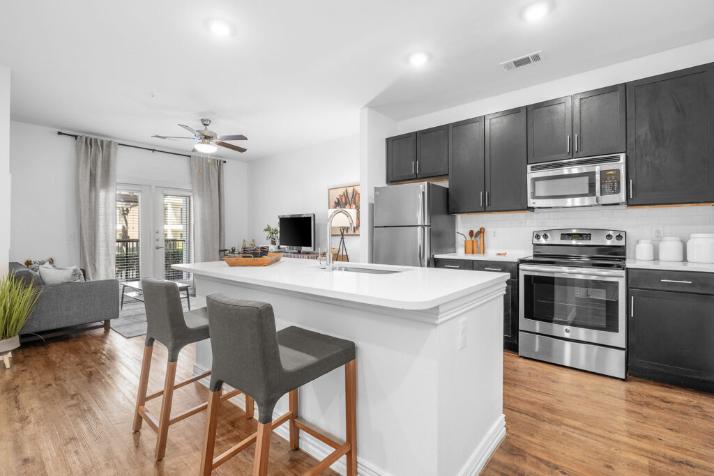 Modern kitchen with dark cabinets, faux-wood flooring, and stainless steel appliances.