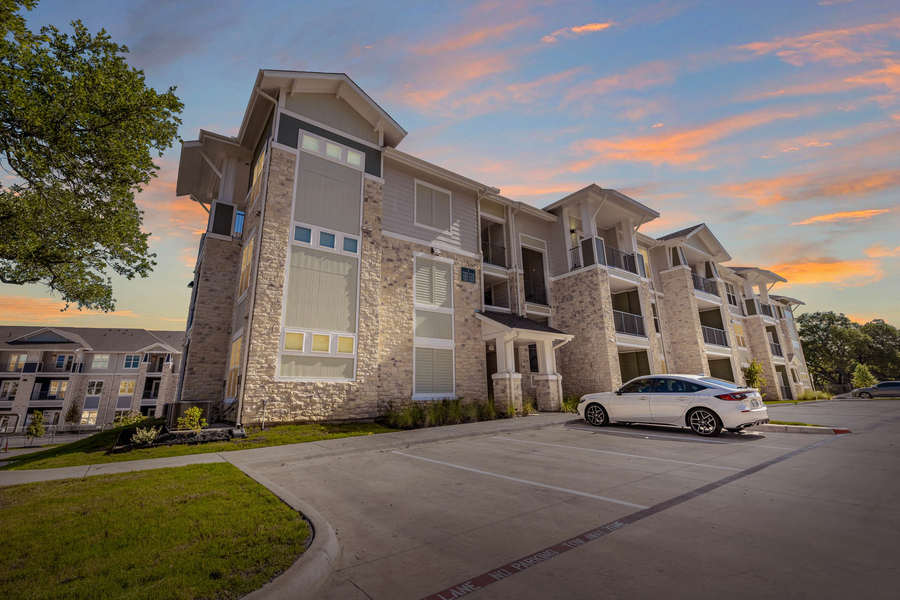 Modern apartment complex with balconies at sunset, parking space in front.