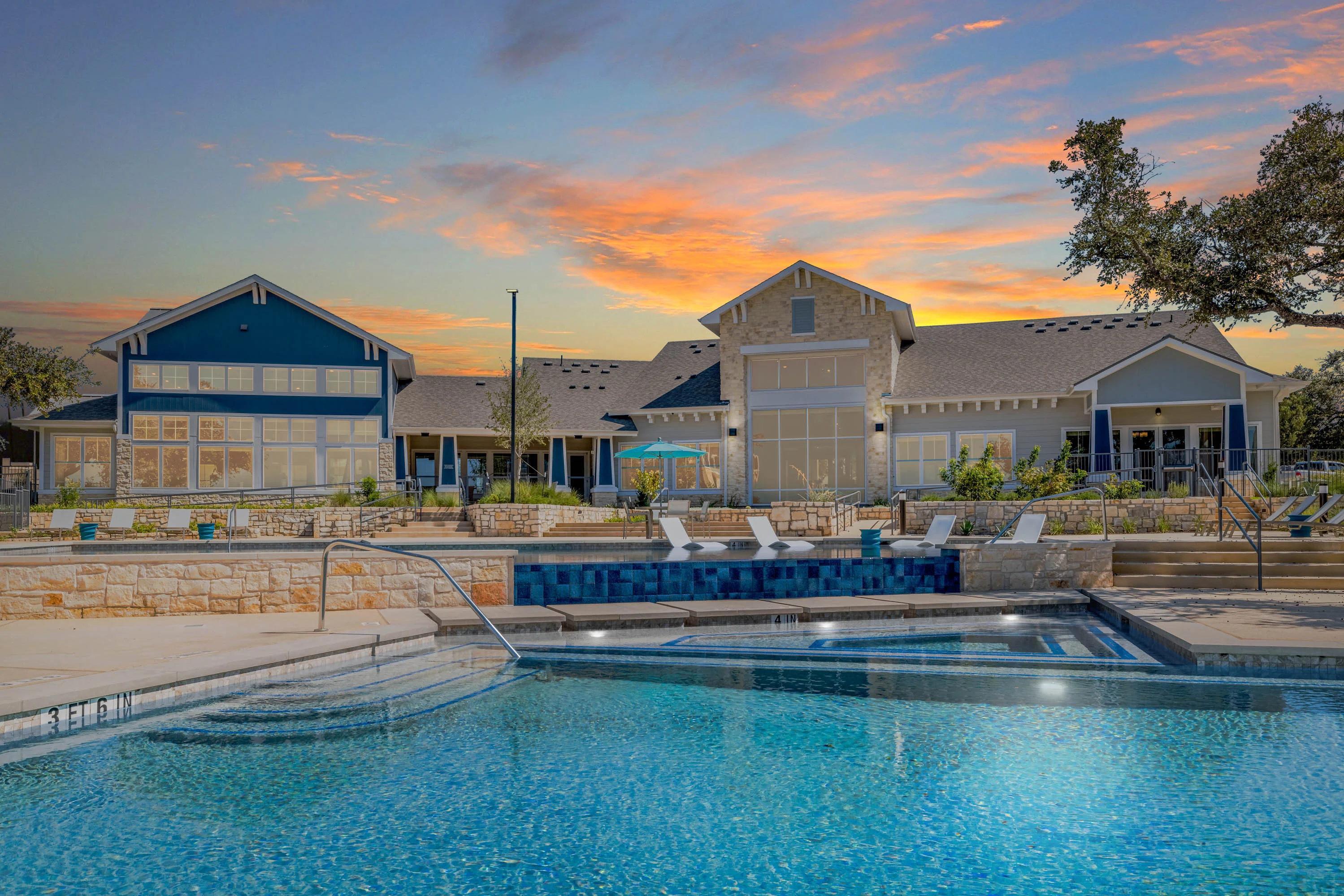 Sunset at an apartment complex with a pool and lounging chairs, surrounded by buildings and trees.