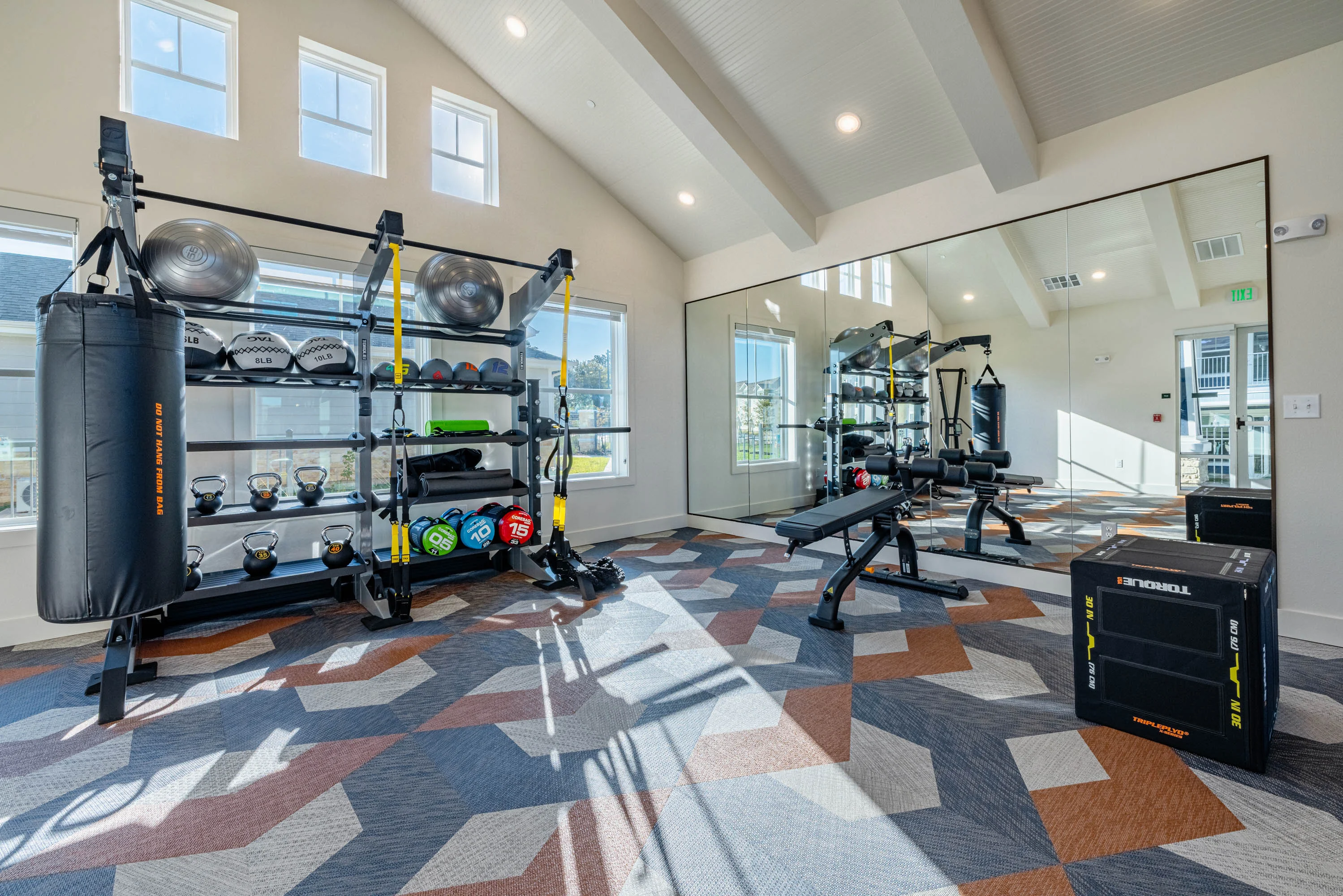 Modern gym room in an apartment complex with exercise equipment and mirrors.
