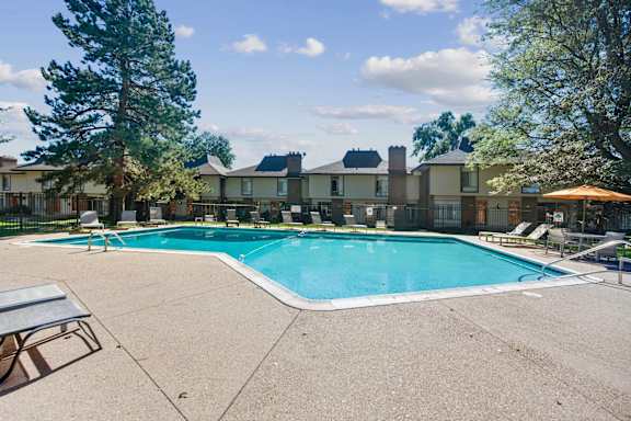 A swimming pool surrounded by a concrete patio and trees. at The Lex At Lowry, Denver, CO, 80224