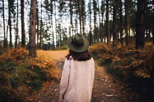 A person in a hat and coat walks down a forest path.