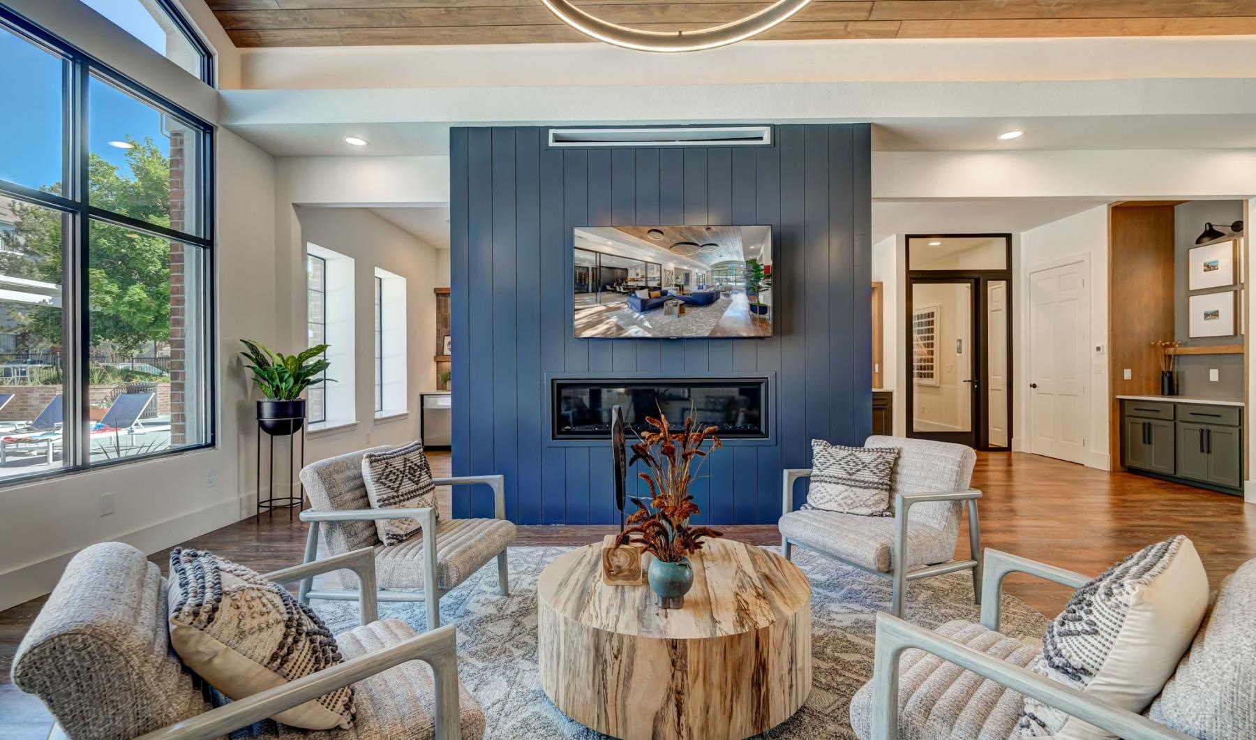 The modern lounge at Cierra Crest Apartments has a blue accent wall with a fireplace and TV, surrounded by armchairs and a circular coffee table.