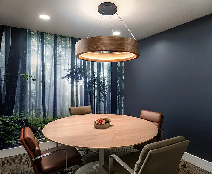 Elegant meeting room with a nature-inspired forest mural, featuring a stylish circular wooden table and modern leather chairs under a chic pendant light.