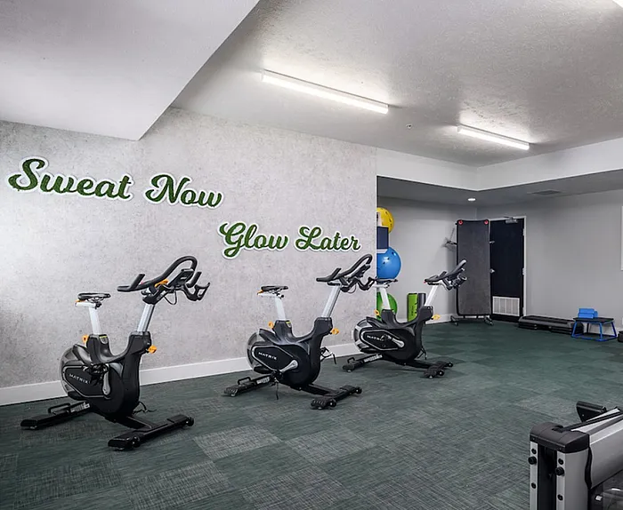 Modern fitness room with exercise bikes and motivational 'Sweat Now, Glow Later' wall art for an energizing workout atmosphere.