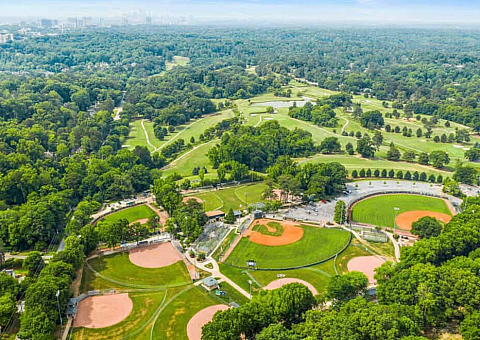 Stunning aerial view of lush green park with multiple baseball fields surrounded by dense forests and vibrant landscapes.