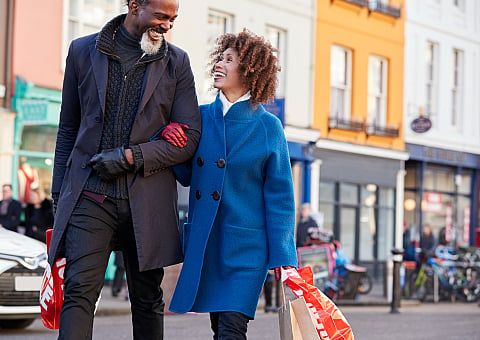 Happy couple strolling arm in arm down a colorful, vibrant street lined with charming buildings and bicycles, enjoying a carefree shopping day.