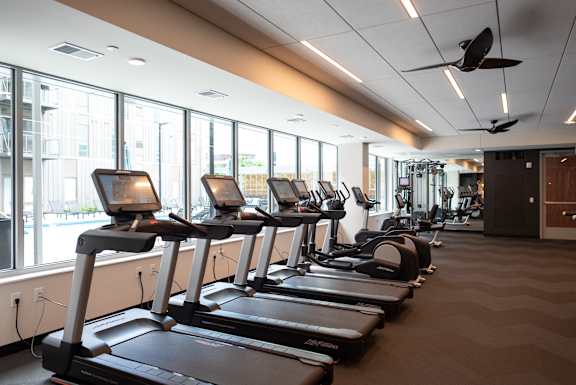 A gym with treadmors and a fan.