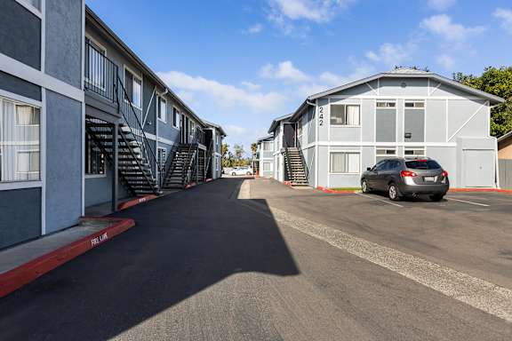 A car is parked in front of a white building with a red stripe on the sidewalk.