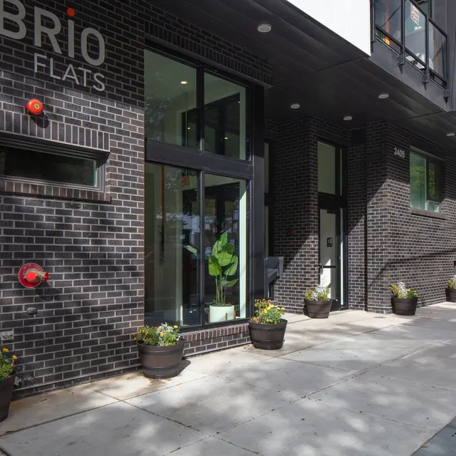 Exterior view of Brio Flats building, featuring a sleek modern design and a landscaped entryway with planters.