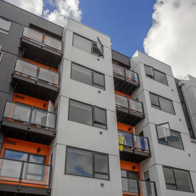 A modern apartment building with a blend of grey and white panels and orange accents on the balconies.