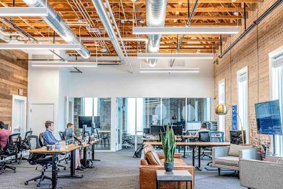 A modern office space with people working at desks and a large window.