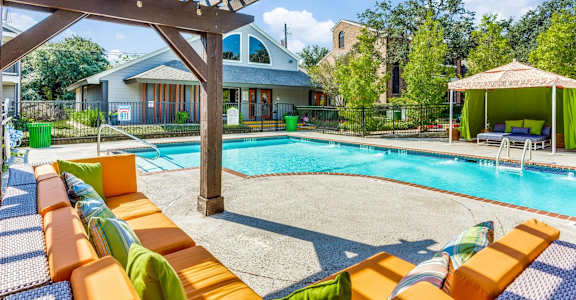 A pool with orange sun loungers and a wooden pergola.
