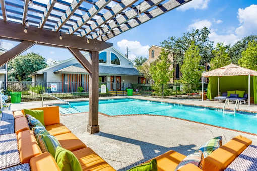 A pool with orange sun loungers and a wooden pergola.