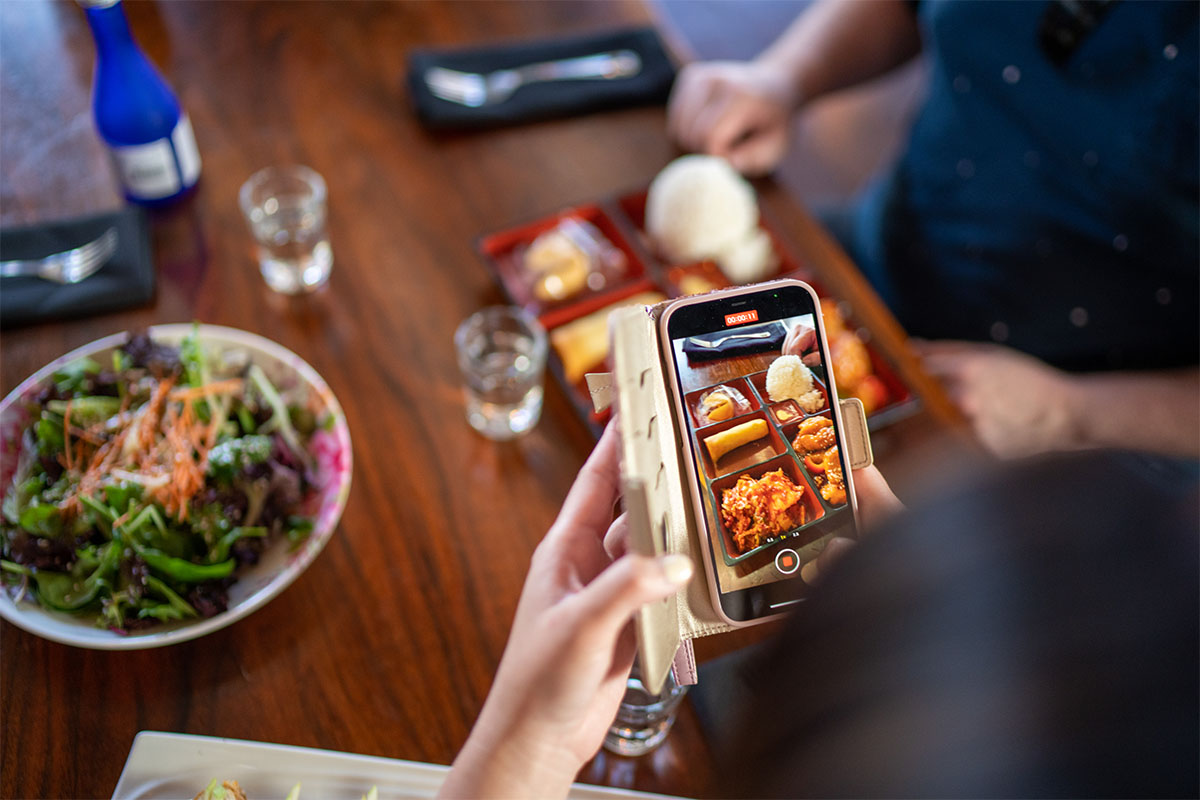Person taking picture of bento box food with smart phone.