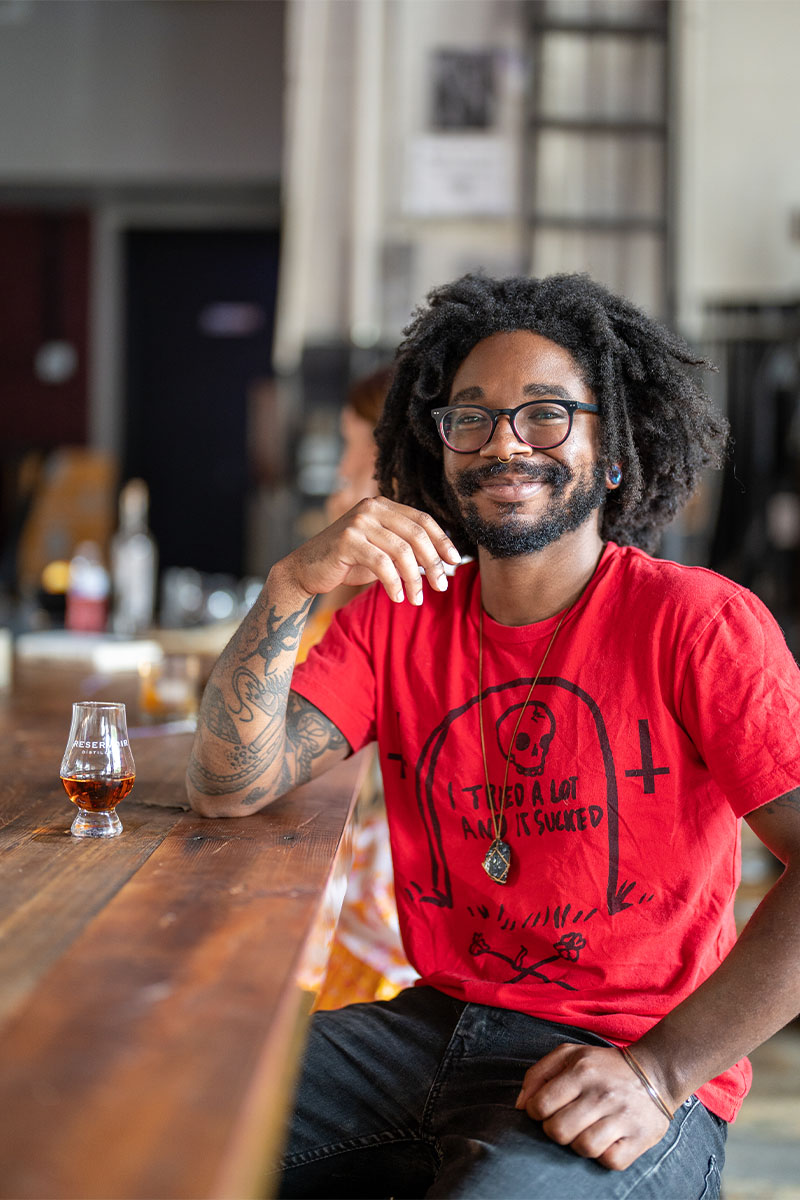 Person in red shirt drinking whiskey at bar.