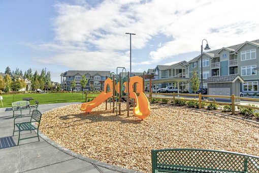 A playground with a slide and a bench in the foreground.