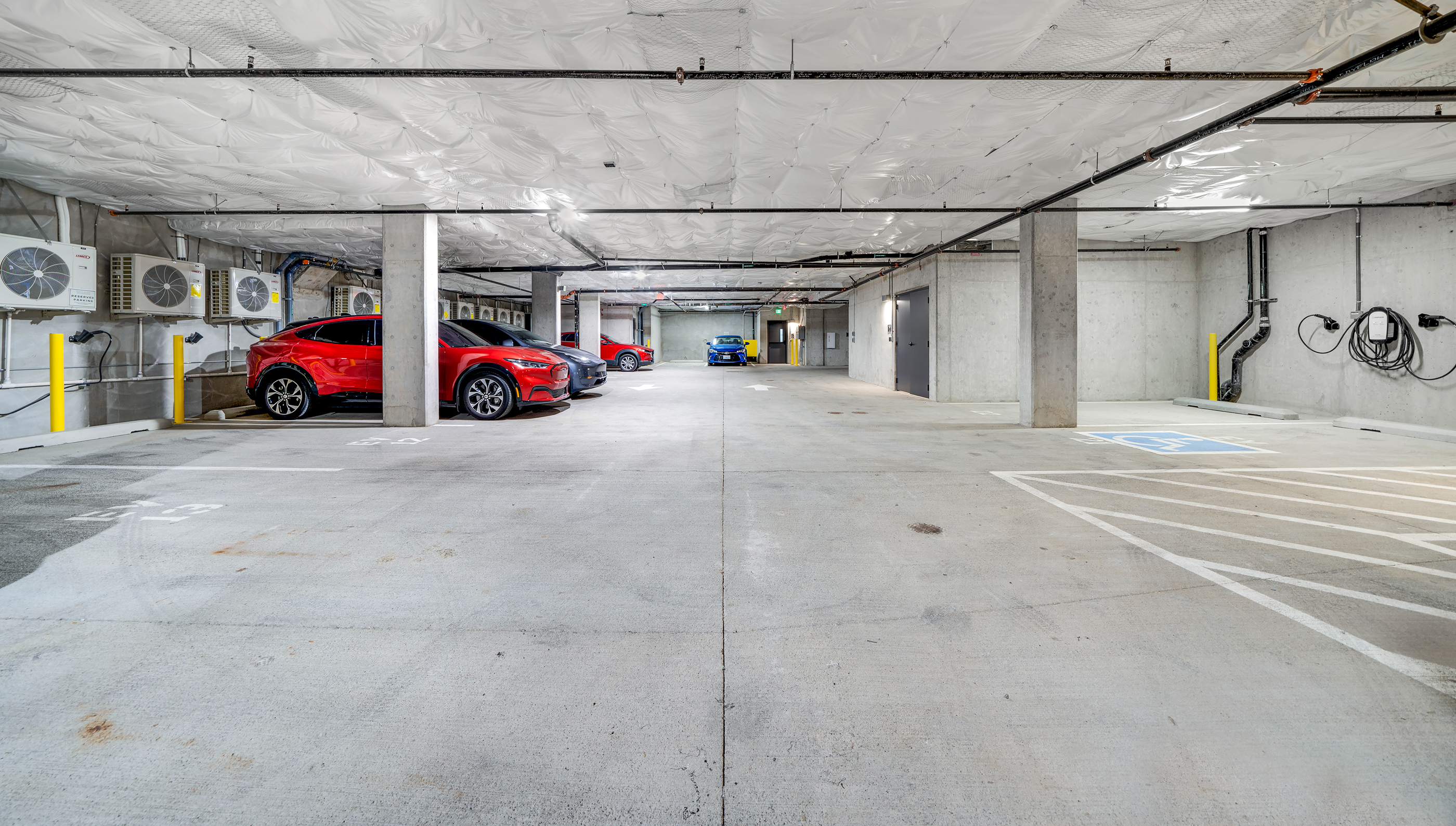 Underground secure parking garage at Capitol Hilltop with a red car parked in it. E/V charging ports on the sides of the garage