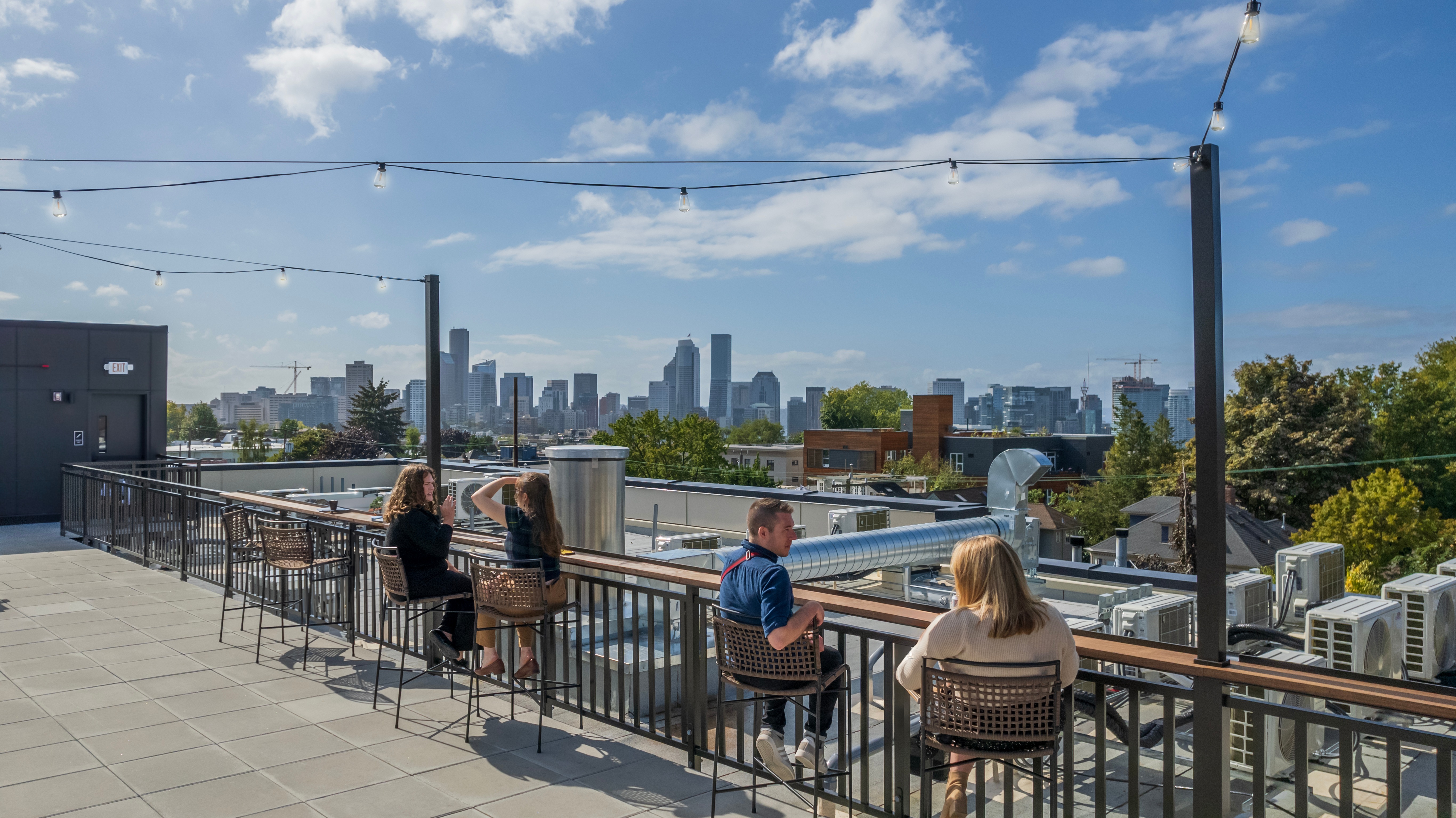 People sitting at bar tables on the Capitol Hilltop Rooftop Skydeck with views of Seattle City Skyline Behind