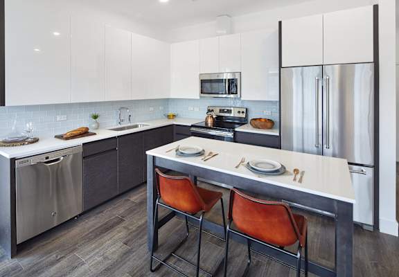 A modern kitchen features sleek white and gray cabinets, stainless steel appliances, and a central island with two orange bar stools.