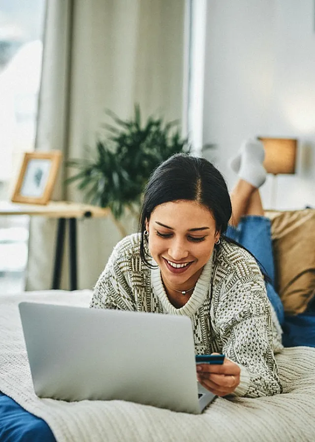 Bright and cozy bedroom with a smiling person on a comfortable bed, using a laptop, surrounded by stylish decor and warm lighting.