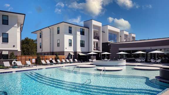 a large swimming pool with lounge chairs and umbrellas in front of a building at Esplanade District Apartments, Little Rock, AR
