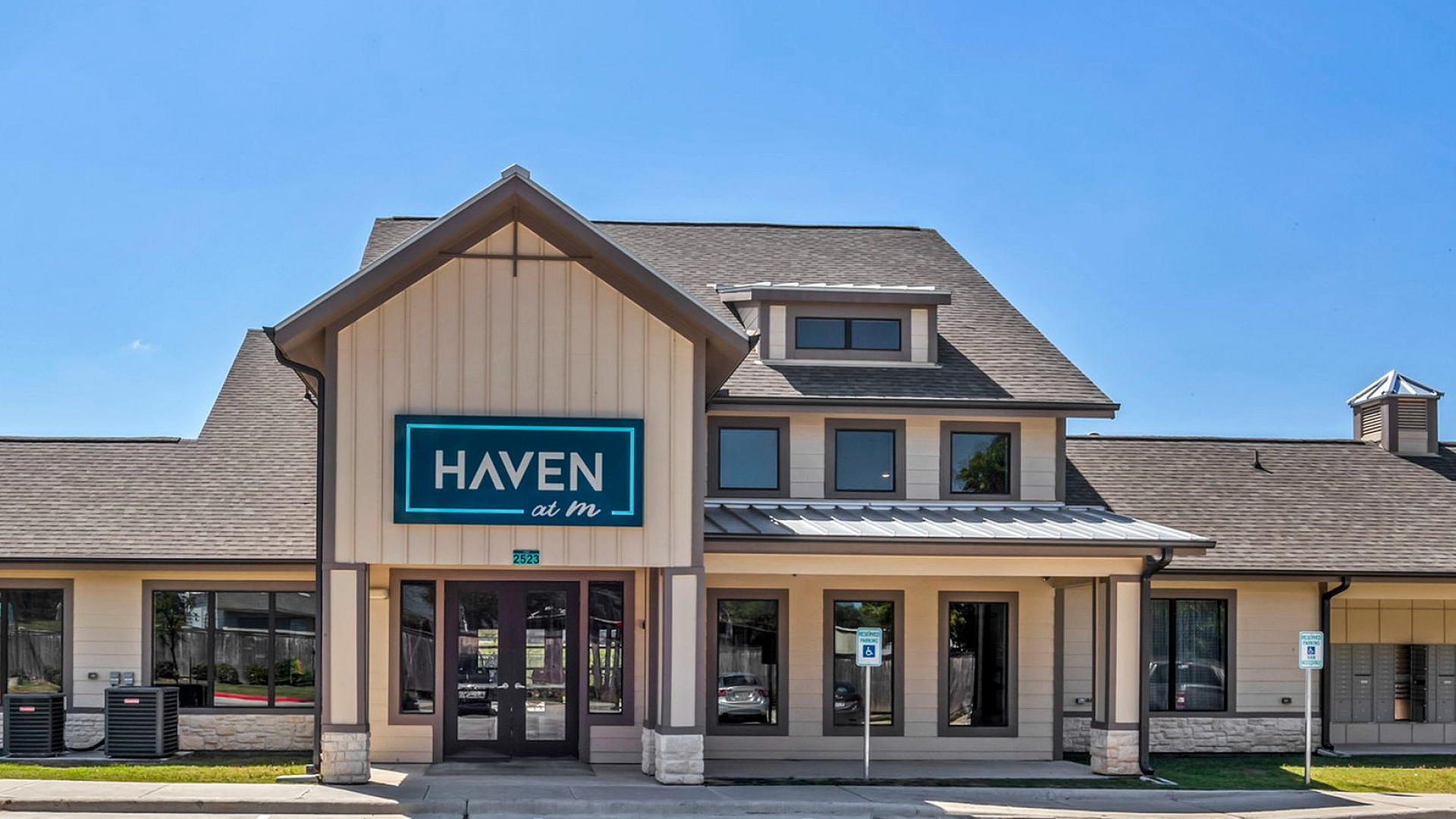 Charming apartment community entrance with modern architecture and welcoming facade under a bright blue sky.