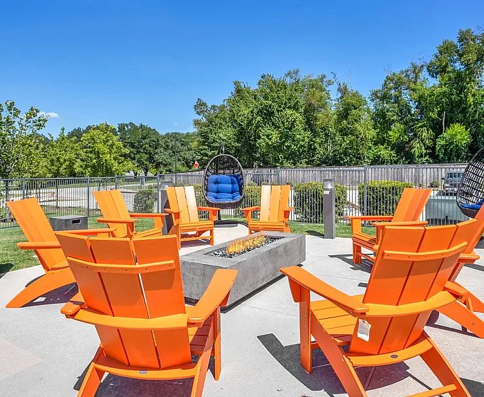 Vibrant outdoor lounge area with bright orange chairs surrounding a modern fire pit, perfect for relaxation and social gatherings.