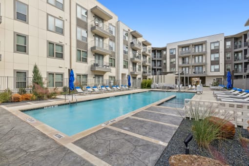 apartment building with a swimming pool and lounge chairs at LynnCora, Grand Prairie, Texas