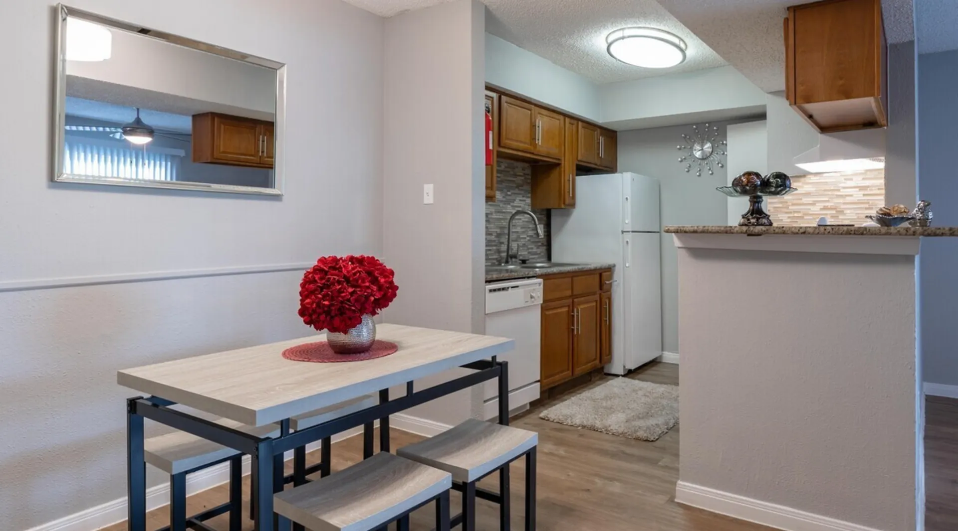 Chic dining area with modern table set, red floral centerpiece, and view of stylish kitchen with wooden cabinets and sleek appliances.