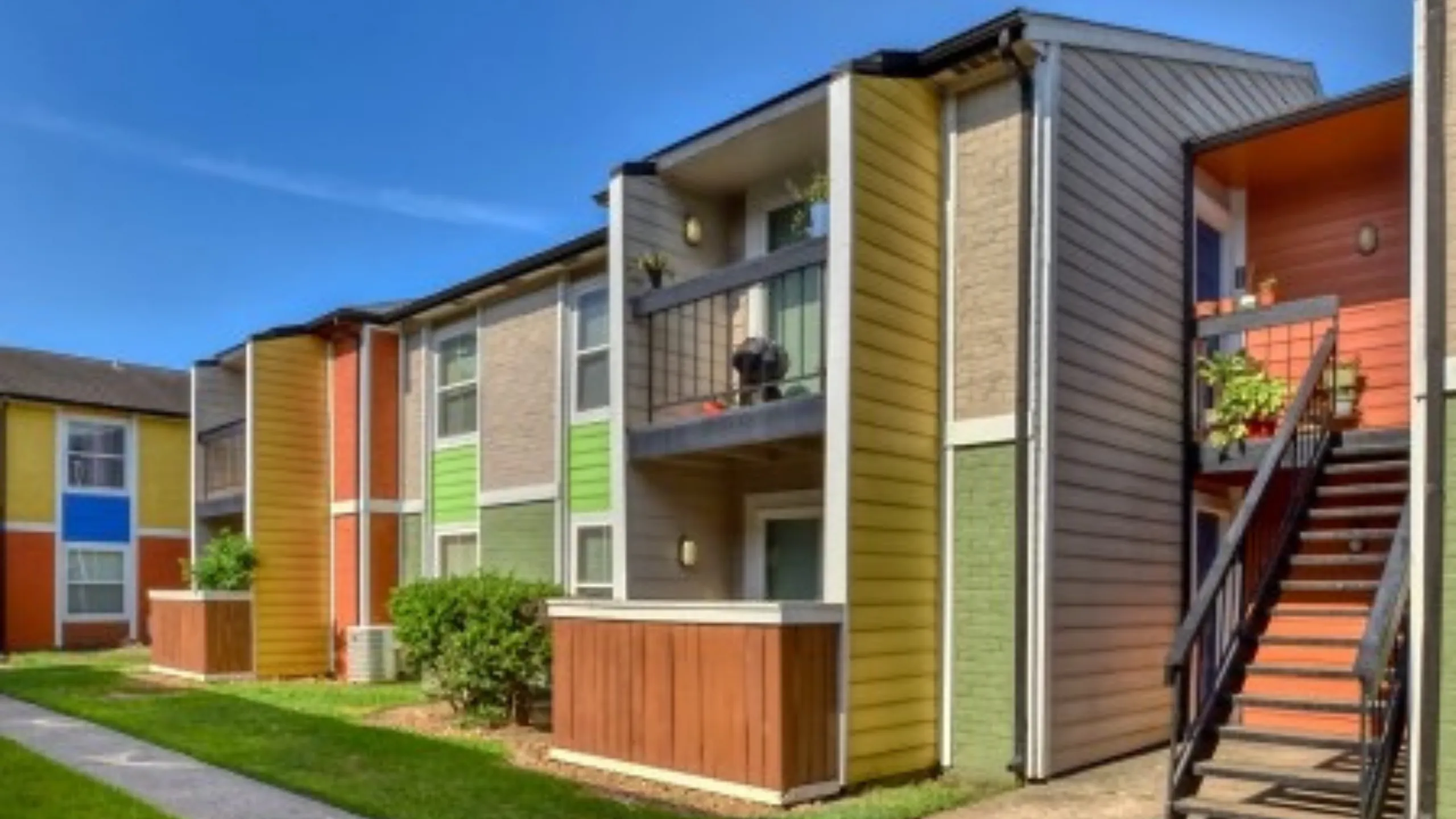 Vibrant apartment exterior featuring colorful paneling, private balconies, and lush greenery.