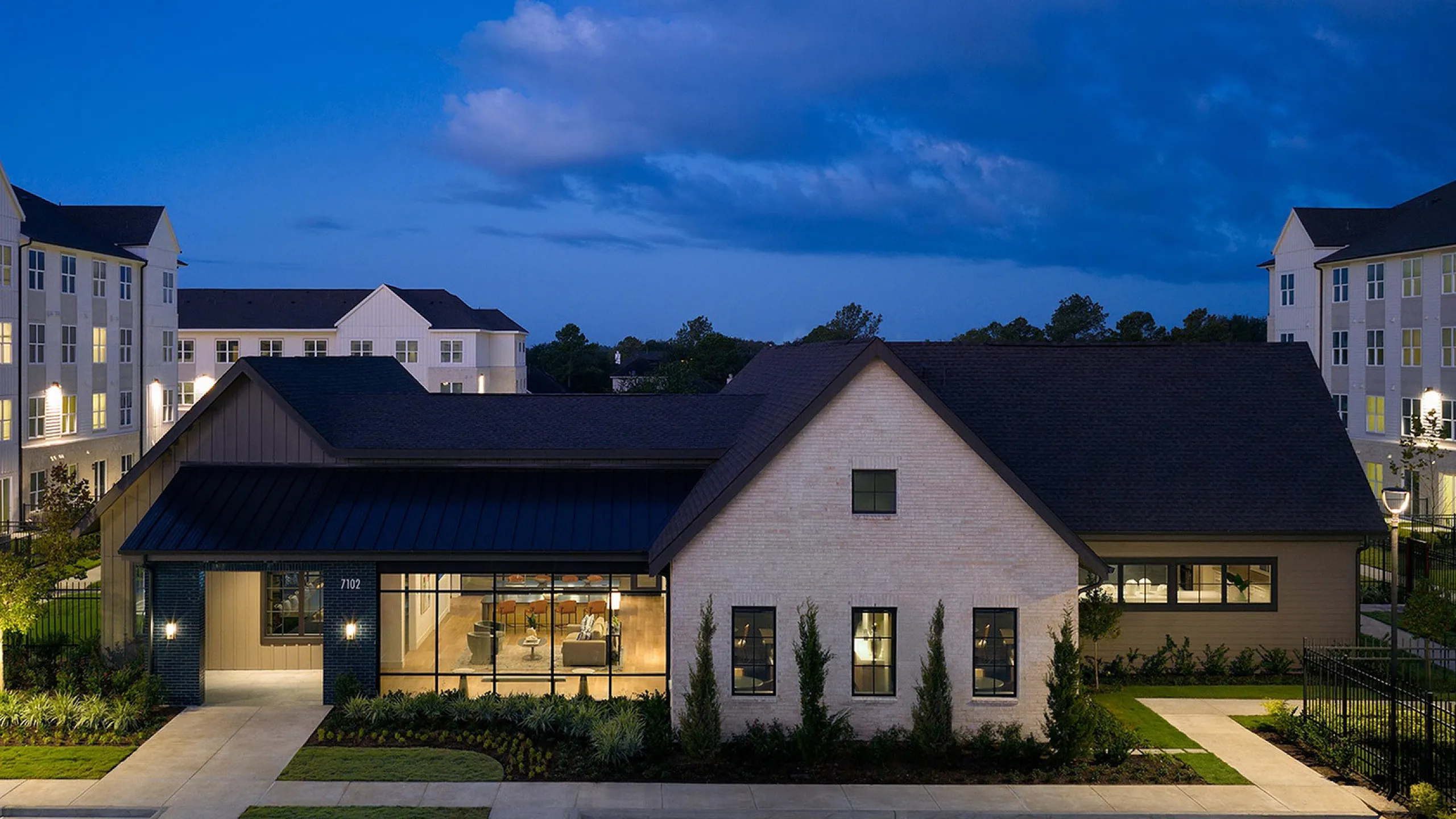 Elegant apartment complex at dusk featuring modern architecture and warm lighting, surrounded by lush landscaping.