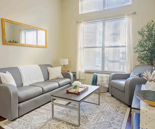 Inviting living room with a modern gray sofa, cozy armchair, and abundant natural light, offering a serene ambiance for relaxation.
