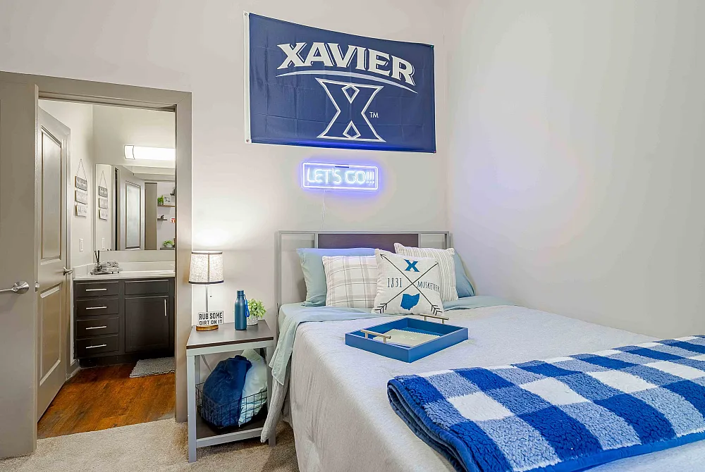 Bright and inviting bedroom featuring a stylish bed with blue accents, adjacent to a modern bathroom, ideal for comfort and relaxation.