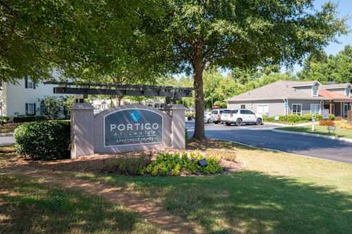 a sign for portico apartments in front of a tree