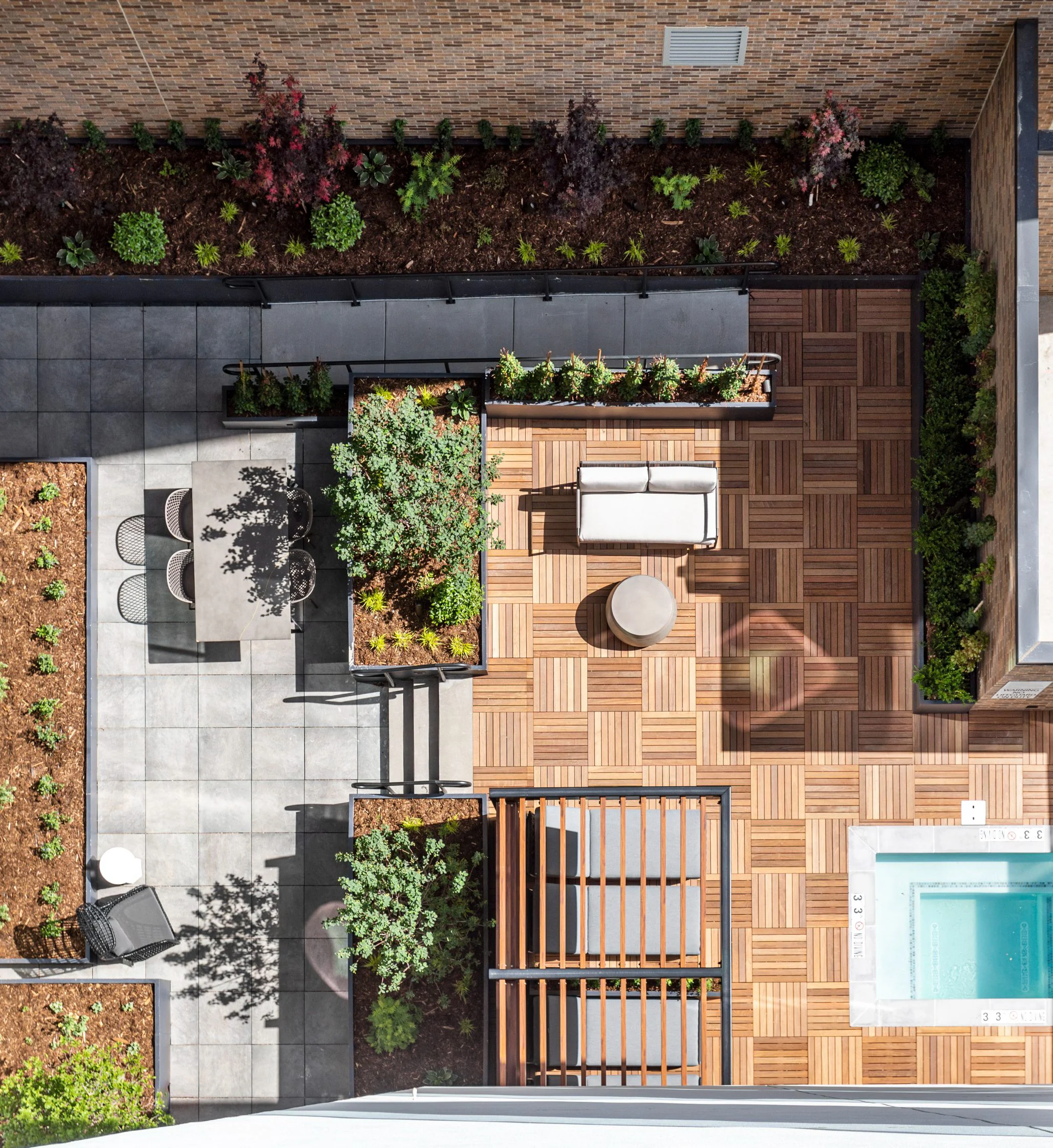An aerial view of a modern rooftop garden featuring a wooden deck, potted plants, a seating area, and a small pool.