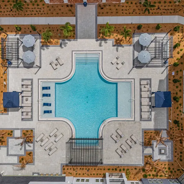 Aerial view of a luxury apartment complex featuring a central swimming pool surrounded by lounge chairs and shaded areas.