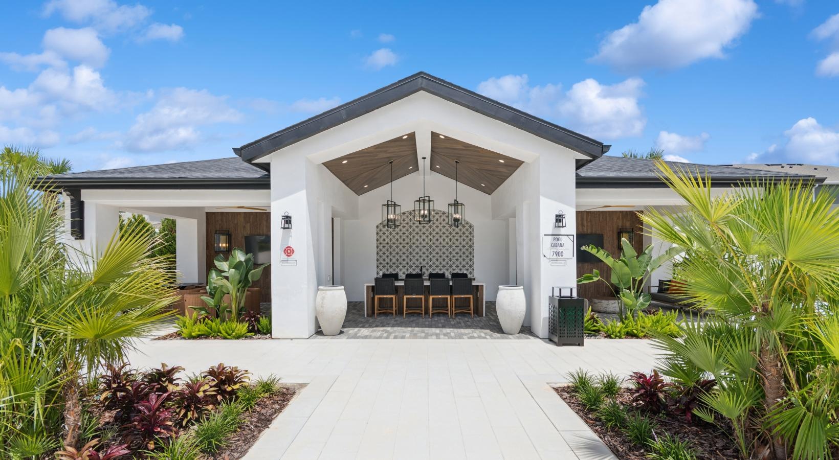 Reunion, FL, Luxury Apartments with In-Unit Washer and Dryer - Ascend Reunion Crossing - Outdoor Lounge Area with a Vaulted Ceiling, Long Table, Chairs, Pendant Lights, and Lush Landscaping.