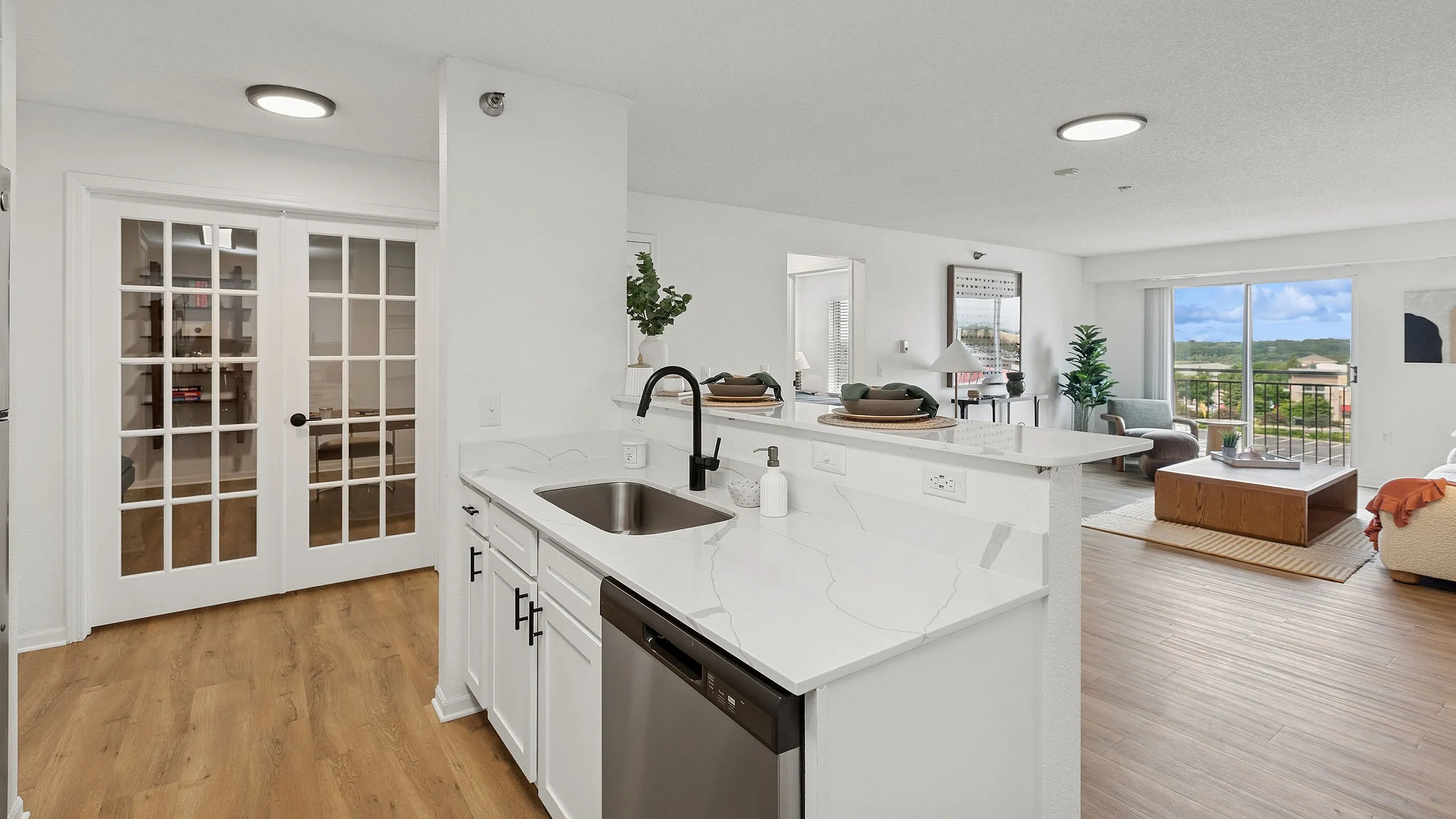 Modern apartment with sleek kitchen featuring marble countertops and stainless steel appliances, opening to a spacious living area with abundant natural light and balcony views.