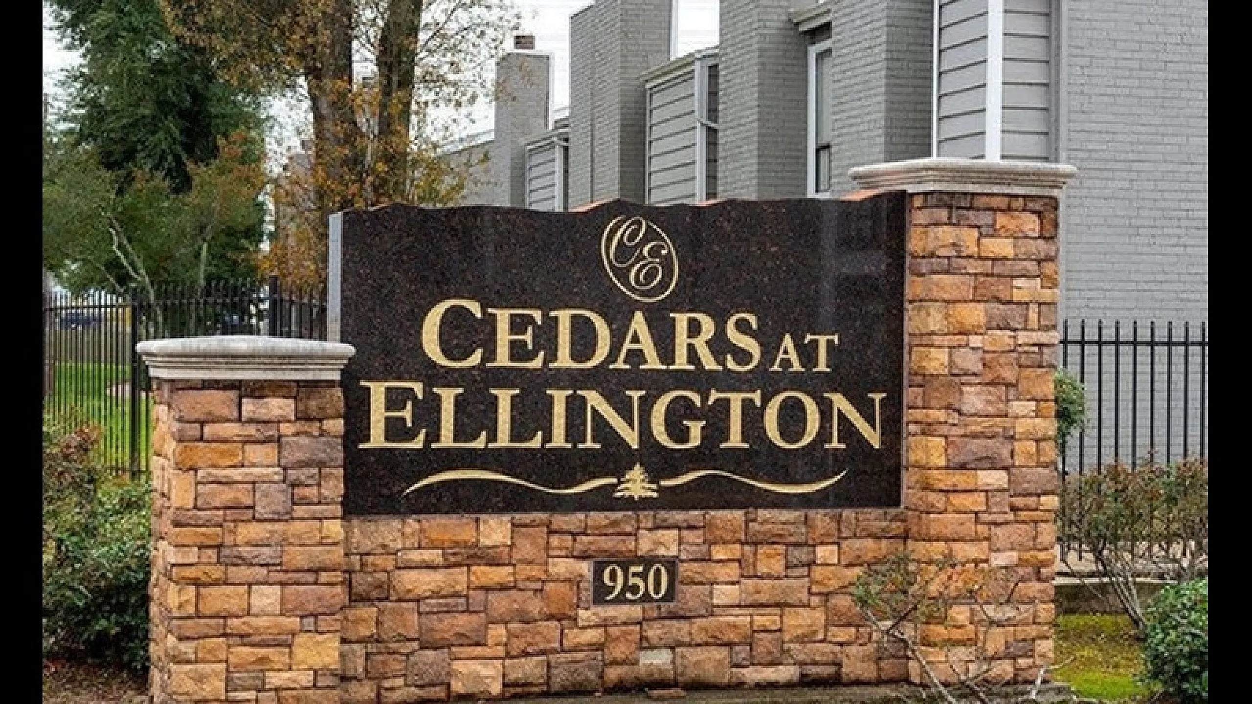 Inviting stone sign for Cedars at Ellington apartment complex surrounded by lush greenery and modern architecture.