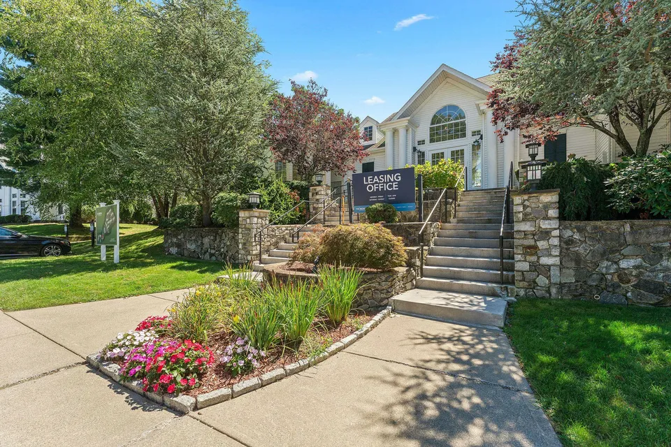 Charming leasing office surrounded by lush greenery and vibrant flowers, showcasing inviting stone steps and classic architecture.