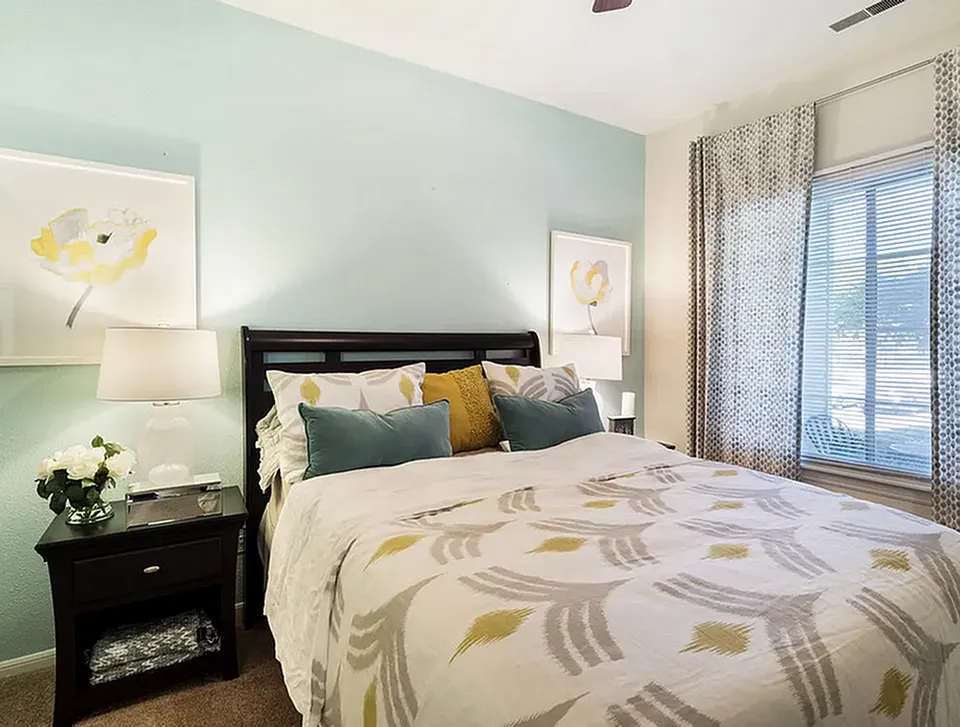 Elegant bedroom with modern decor, featuring a plush bed adorned with stylish cushions, ambient lighting, and a serene palette.
