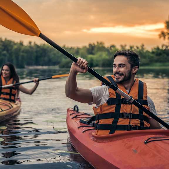 Two people kayaking on a lake at sunset.
